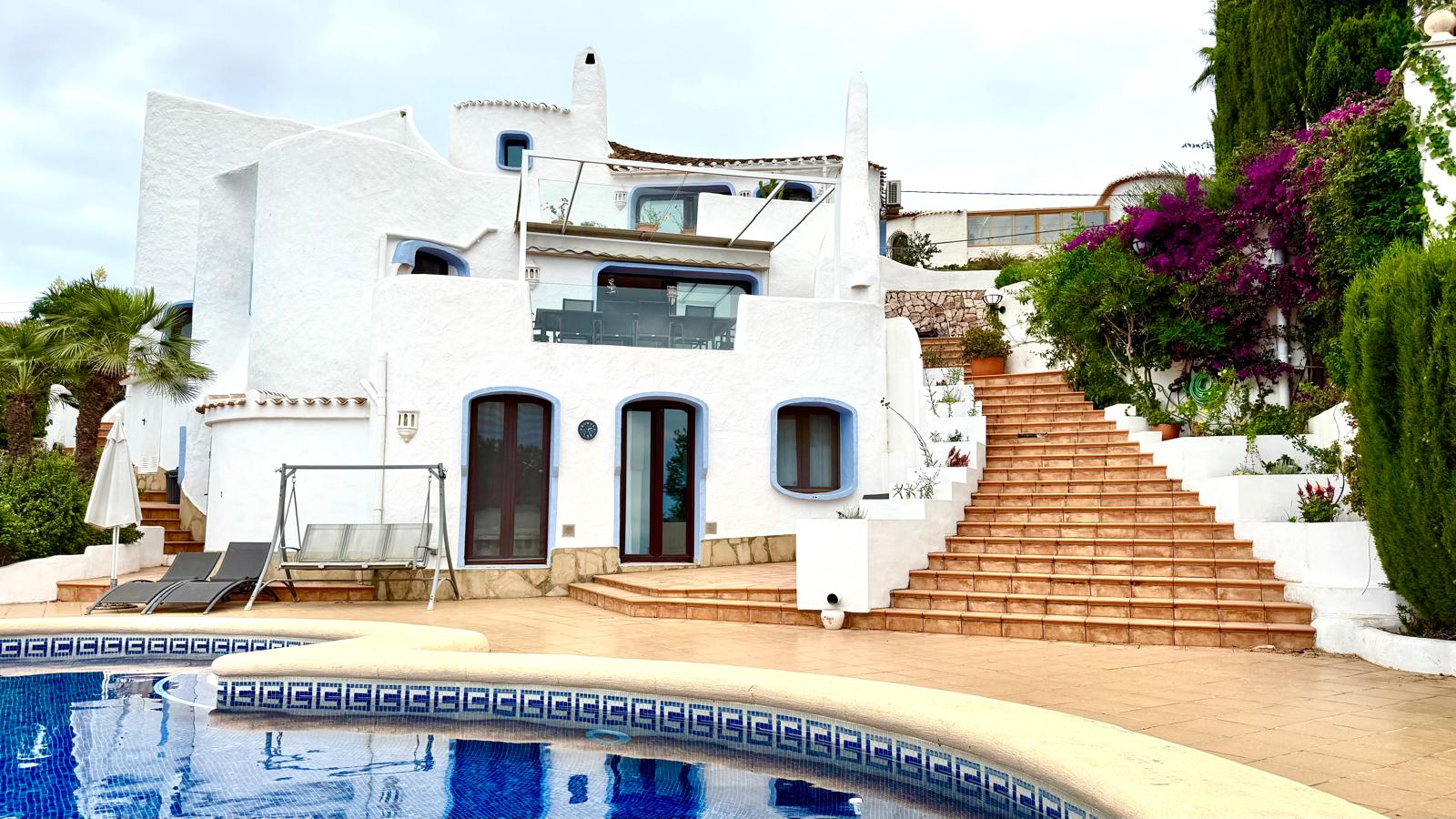 Façade blanche de style ibizien avec menuiseries bleues, terrasse en terre cuite et large escalier extérieur menant aux différents niveaux depuis la piscine privée.