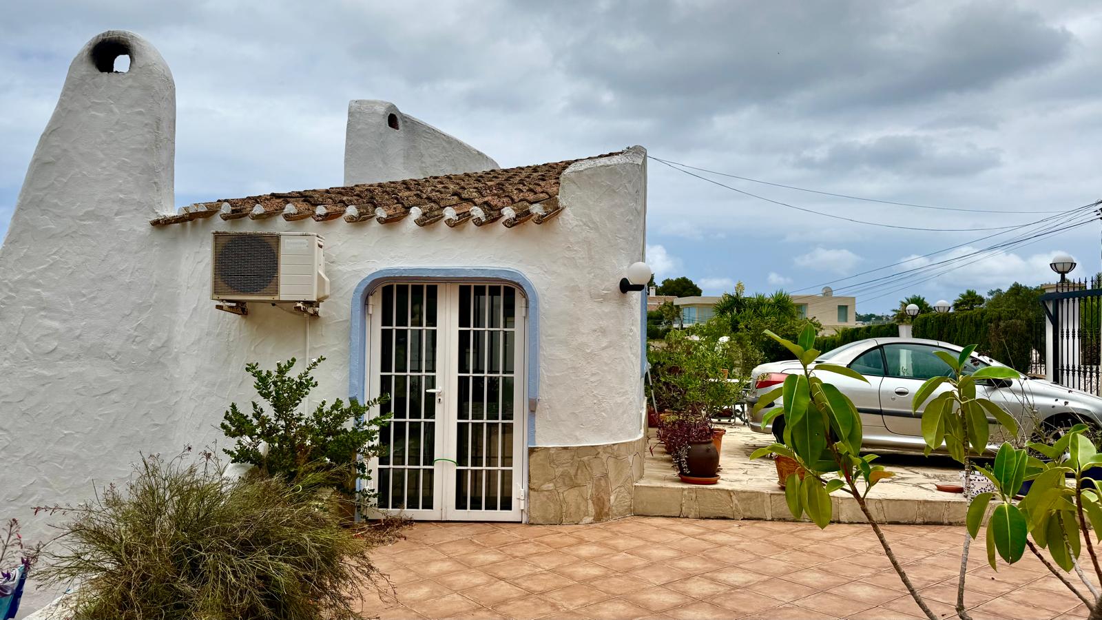 Façade de style Ibiza aux murs blancs arrondis, cheminées traditionnelles et soubassement en pierre. Comprend une zone de stationnement de plain-pied et une terrasse carrelée.