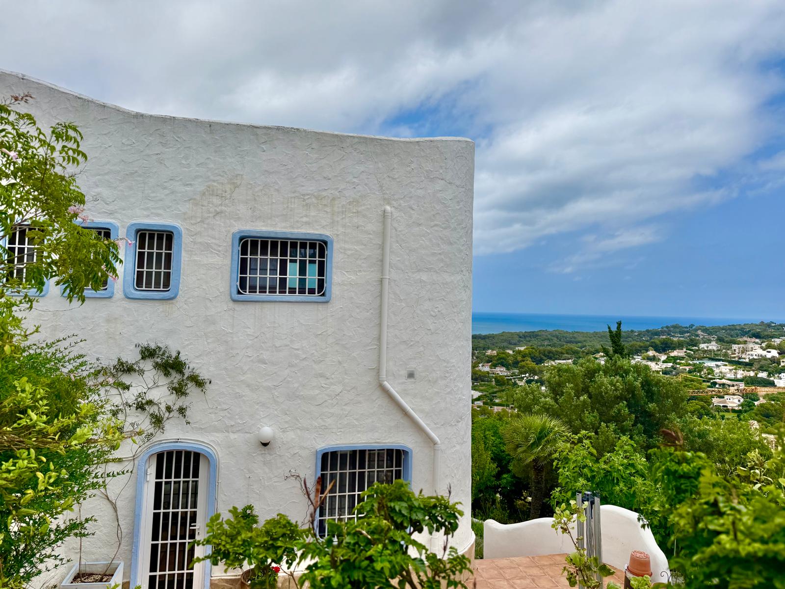 Façade de style ibizien aux murs blancs et encadrements bleus, offrant une vue panoramique sur la mer Méditerranée et la côte de Jávea.