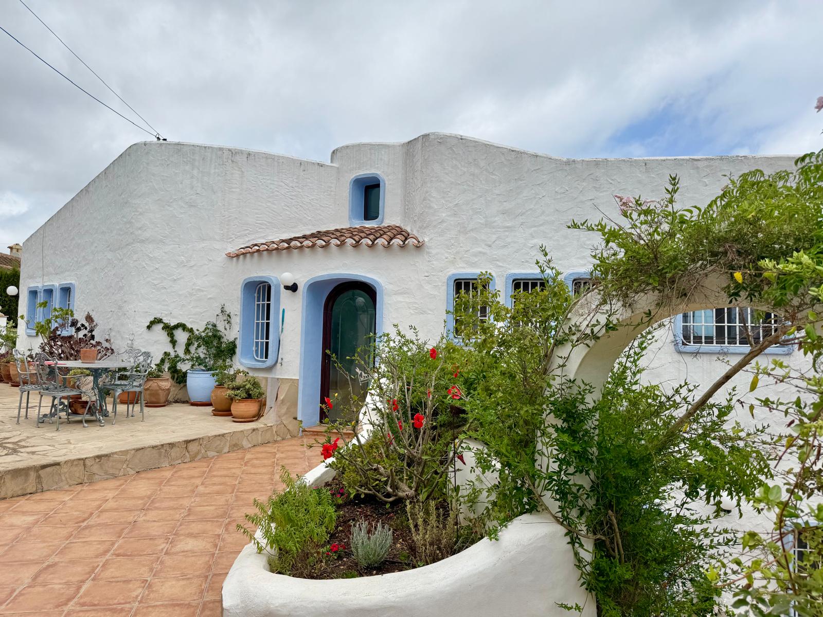 Façade de style ibizien aux murs blancs et menuiseries bleues, complétée par une terrasse en terre cuite et des jardinières maçonnées avec flore locale.