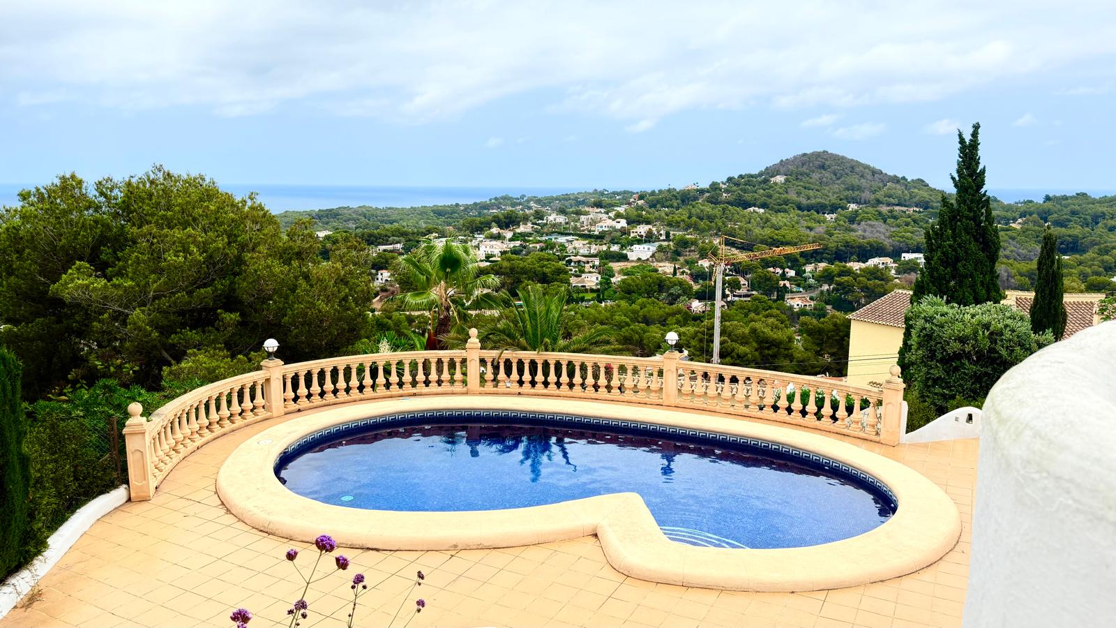 Piscine de forme incurvée entourée d'une terrasse carrelée et d'une balustrade classique, offrant une vue panoramique sur la mer Méditerranée et Jávea.