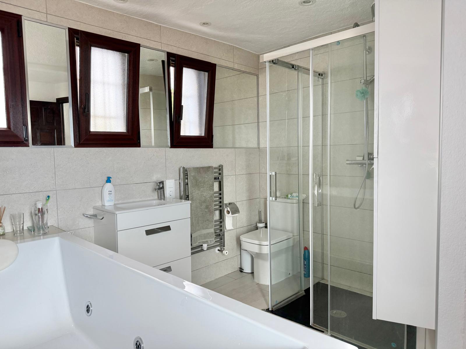 Salle de bain équipée d'une baignoire d'hydromassage, d'une douche vitrée, d'un meuble vasque blanc et d'un radiateur sèche-serviettes mural.