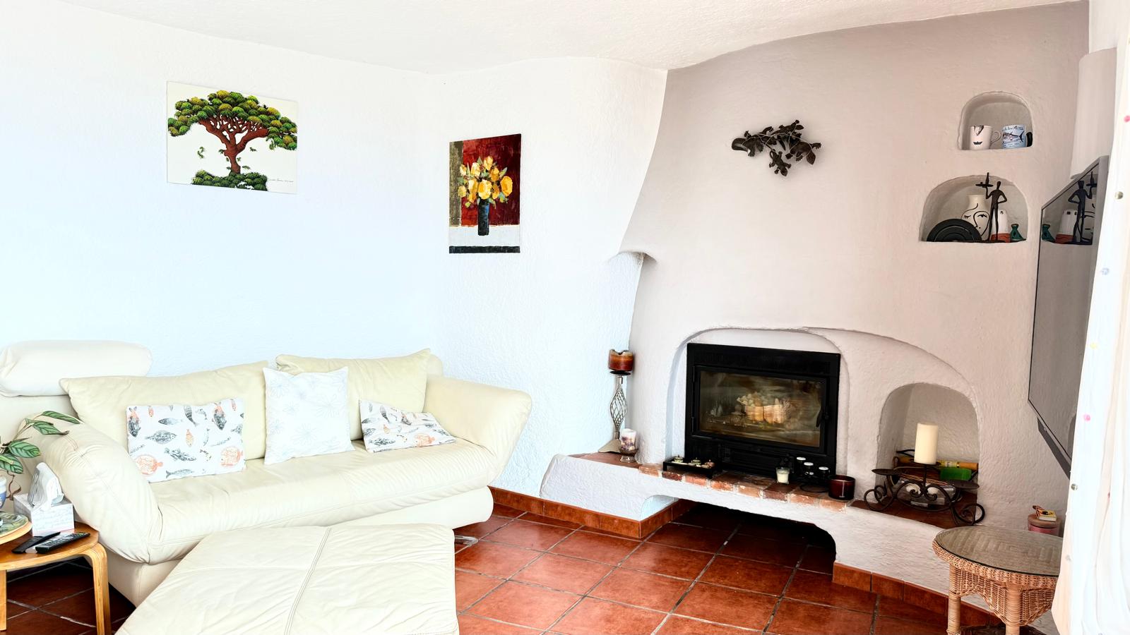 Salon de style ibizane avec cheminée à insert, niches décoratives intégrées dans le mur, sol en terre cuite et murs blancs aux formes organiques.