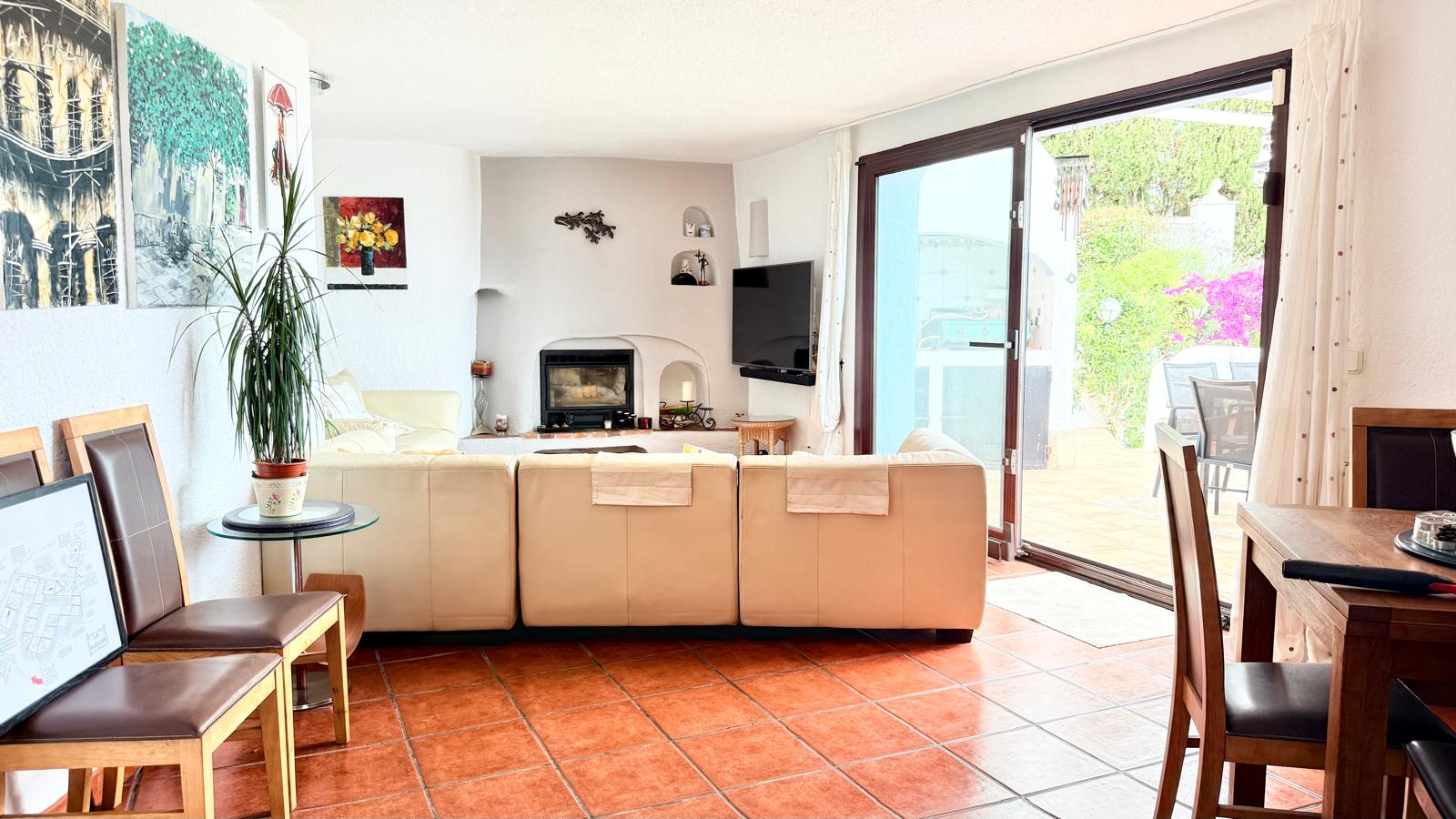 Salon-salle à manger avec cheminée à bois intégrée, sol en grès rustique et grande baie vitrée coulissante offrant un accès direct vers la terrasse extérieure.