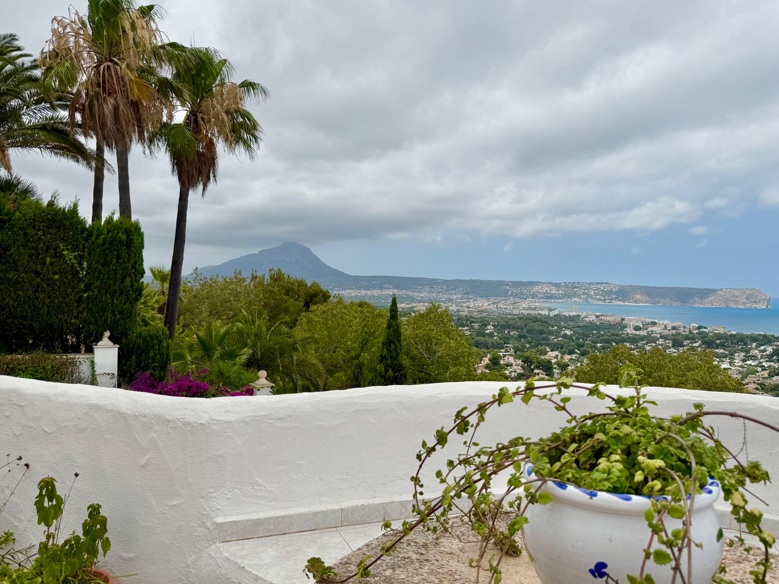 Vue panoramique depuis la terrasse sur la baie de Jávea et le Montgó, encadrée par une végétation méditerranéenne et des murs blancs de style ibizien.