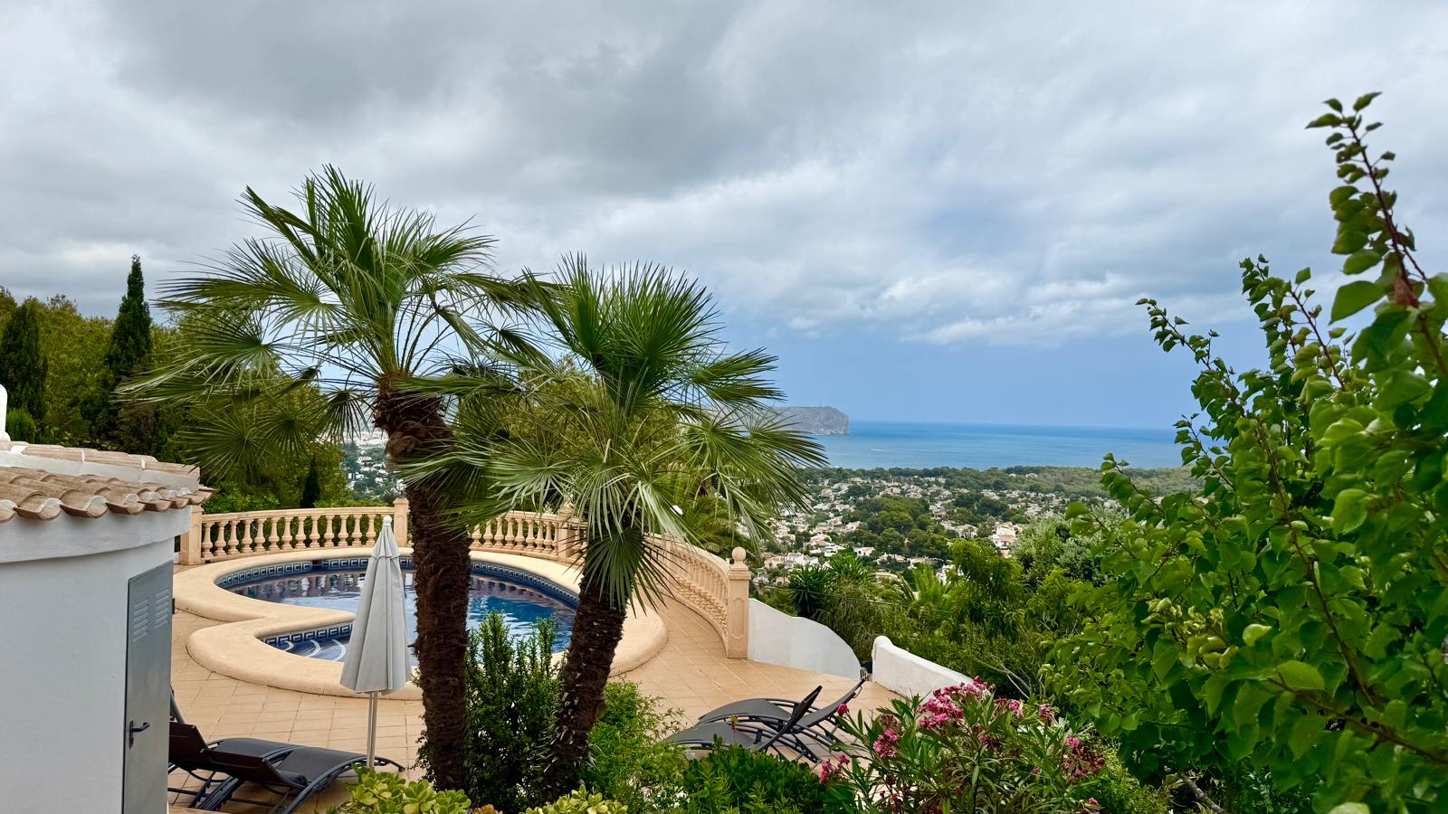 Vue surélevée de la piscine aux formes courbes et du jardin méditerranéen, offrant un panorama sur la baie de Jávea et le littoral depuis la terrasse.