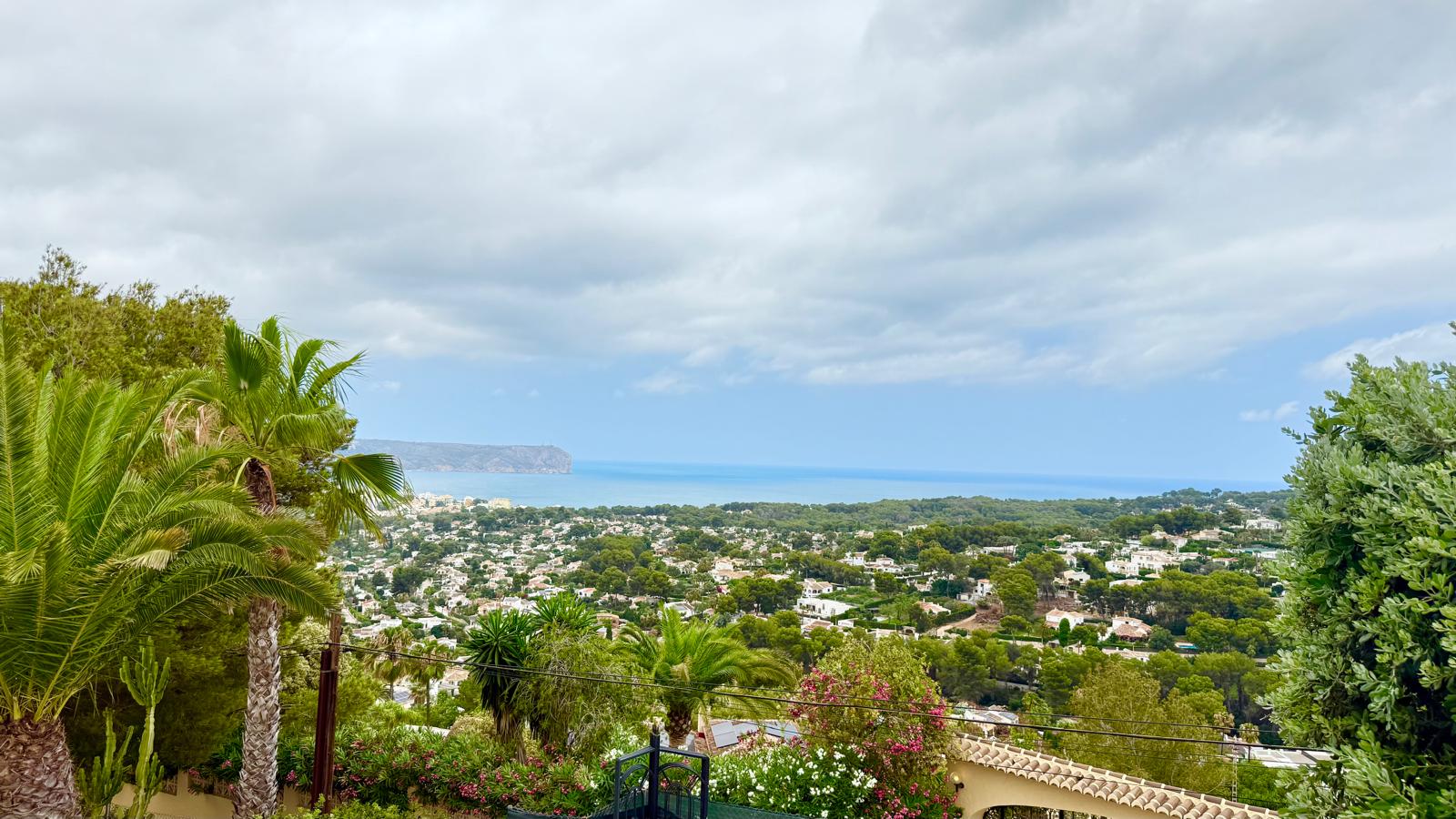 Vues panoramiques sur la baie de Jávea et la mer Méditerranée depuis la position surélevée de la villa, entourée de palmiers et de verdure.
