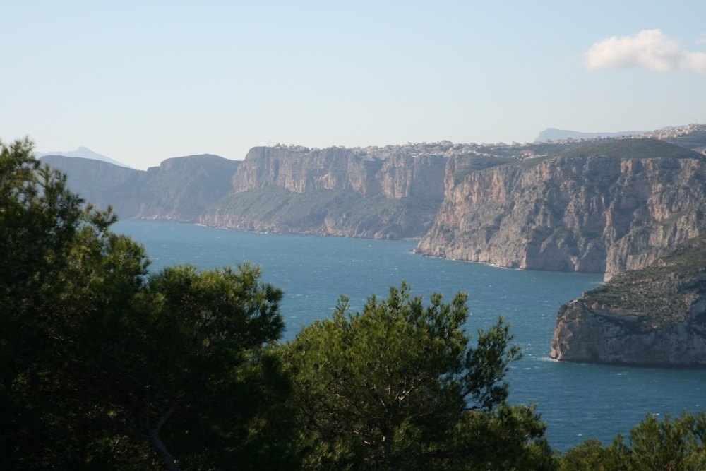 Vues panoramiques sur la mer Méditerranée et les falaises escarpées de la côte de Jávea, encadrées par des pins indigènes sous un ciel dégagé.