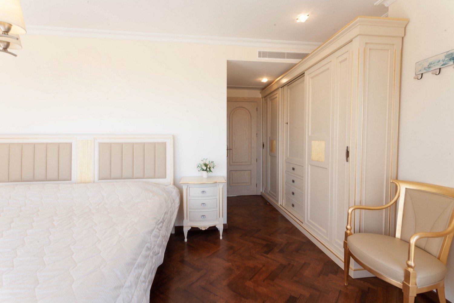 Chambre avec lit à tête de lit rembourrée, armoire intégrée en bois clair et parquet foncé.