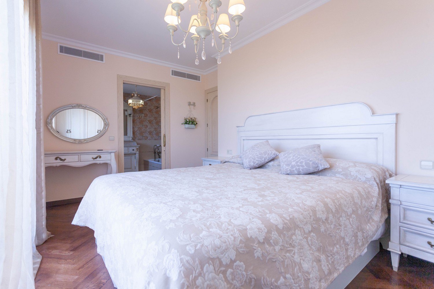 Chambre avec lit double, coiffeuse avec miroir ovale et salle de bain attenante avec papier peint à motifs.