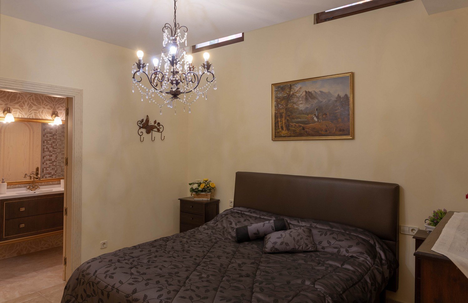 Chambre avec lit double, lustre en cristal et accès à une salle de bain attenante avec double vasque.