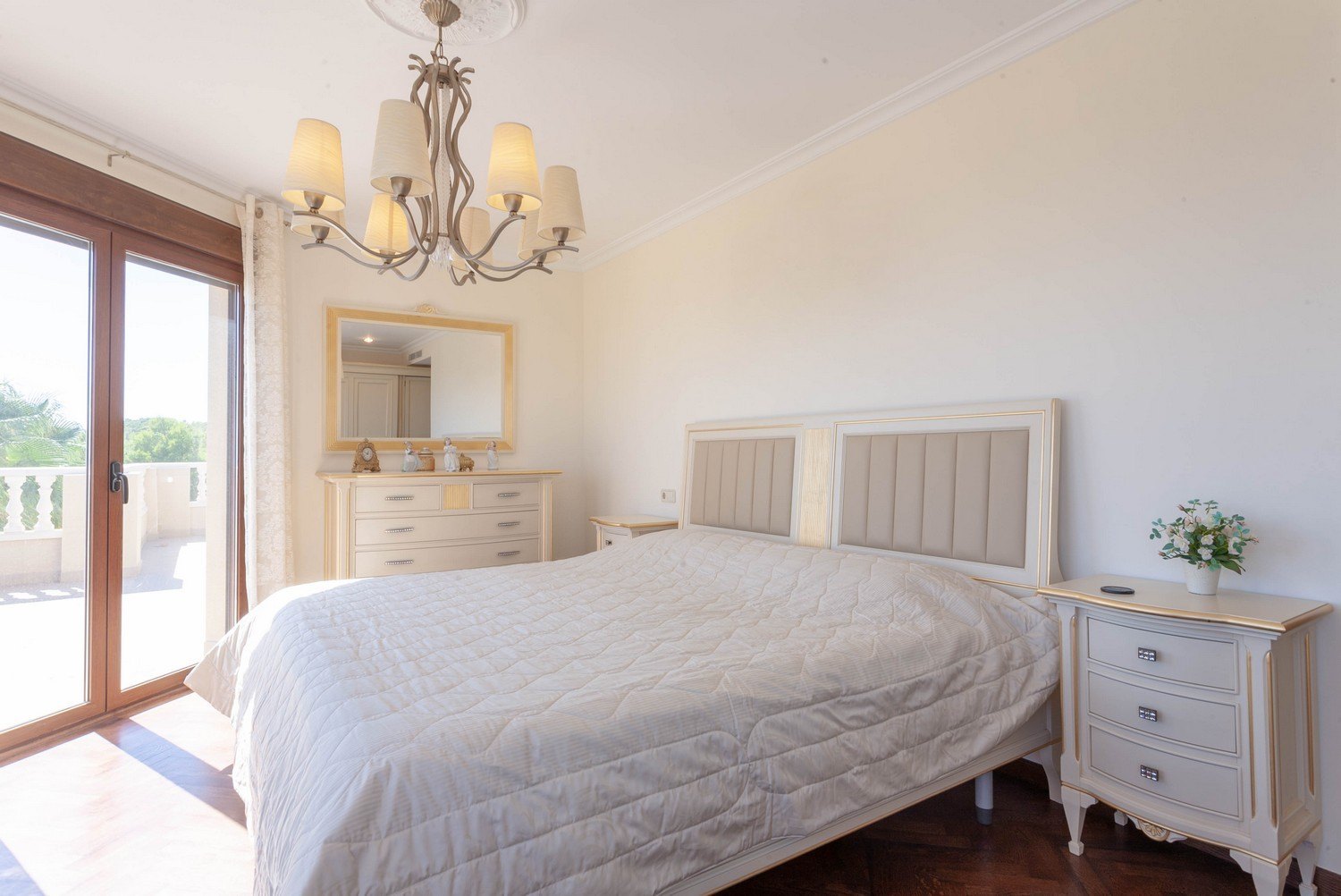 Chambre lumineuse avec lit double, tables de chevet et commode classique avec miroir à cadre doré.