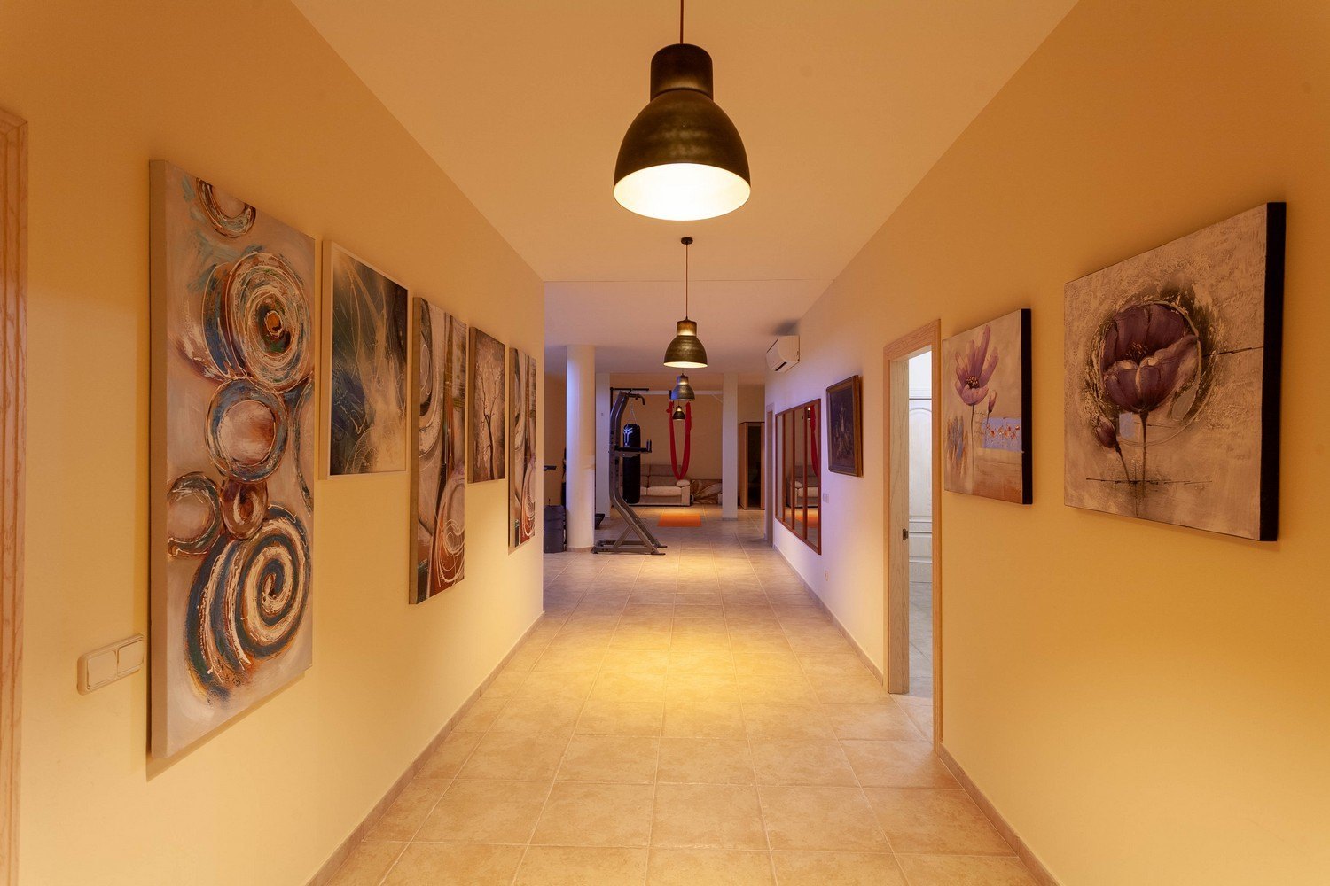 Couloir illuminé avec des œuvres d'art et accès à la salle de sport.