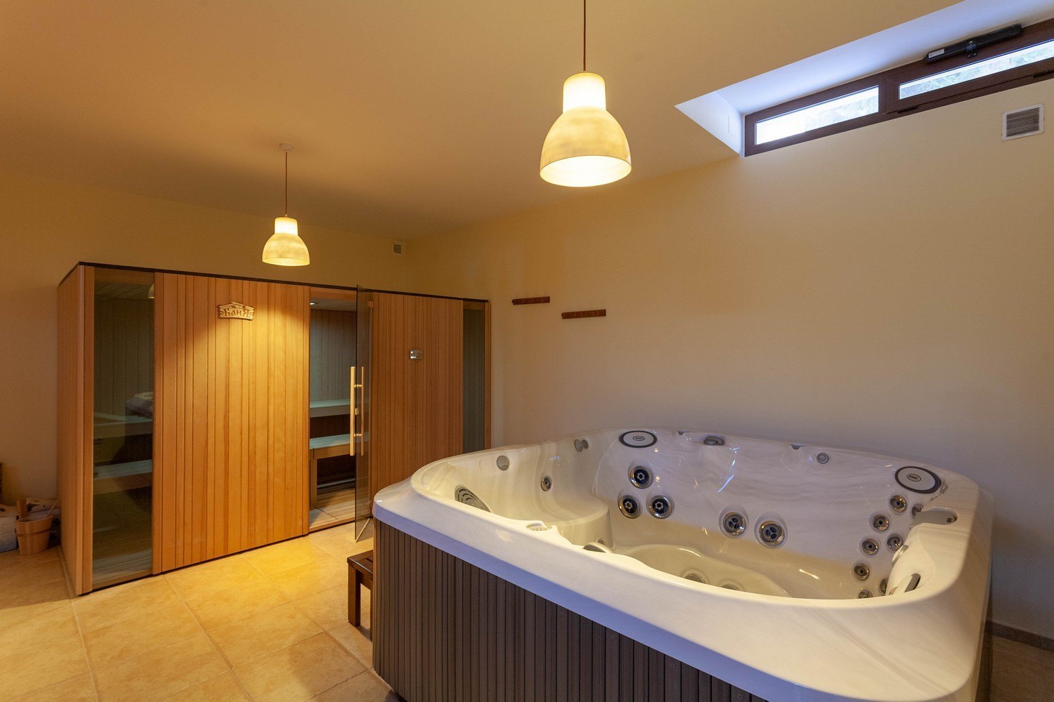 Détail du jacuzzi et du sauna en bois clair avec porte en verre.
