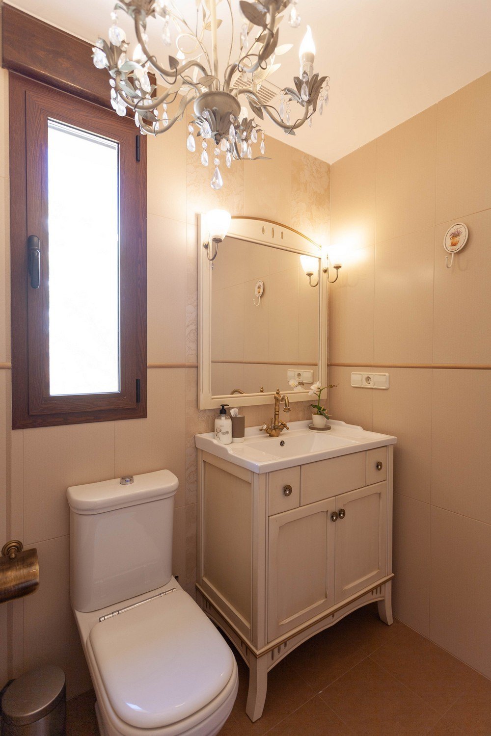 Détail d'une salle de bain classique avec meuble-lavabo en bois et comptoir blanc, miroir avec appliques et lustre en cristal.
