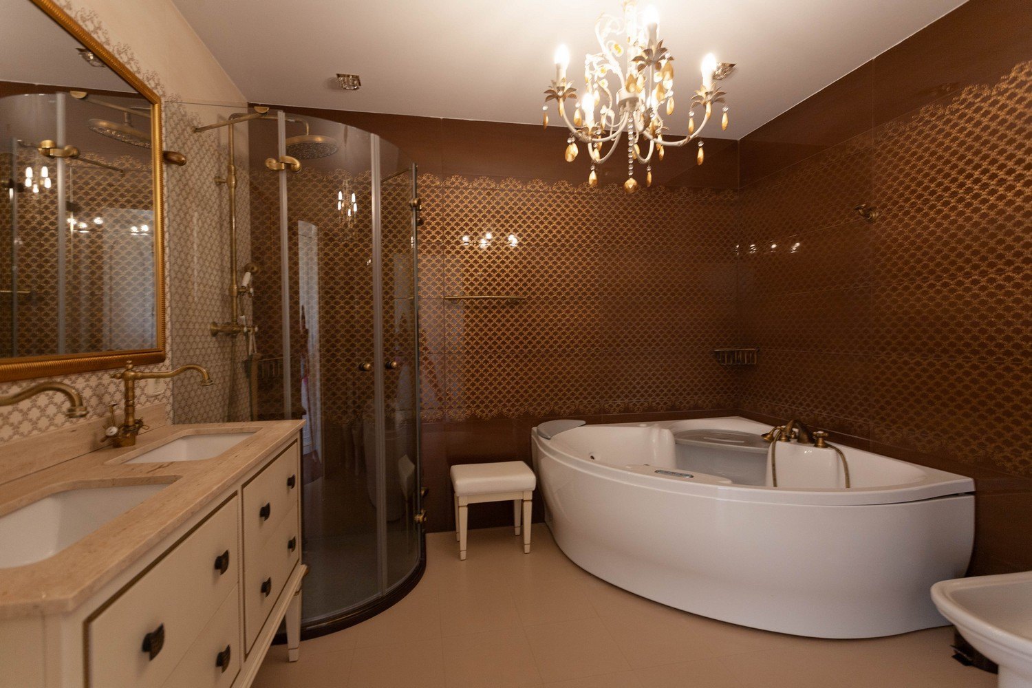 Élégante salle de bain avec baignoire balnéo, douche en verre courbé et meuble-lavabo double avec robinetterie dorée.
