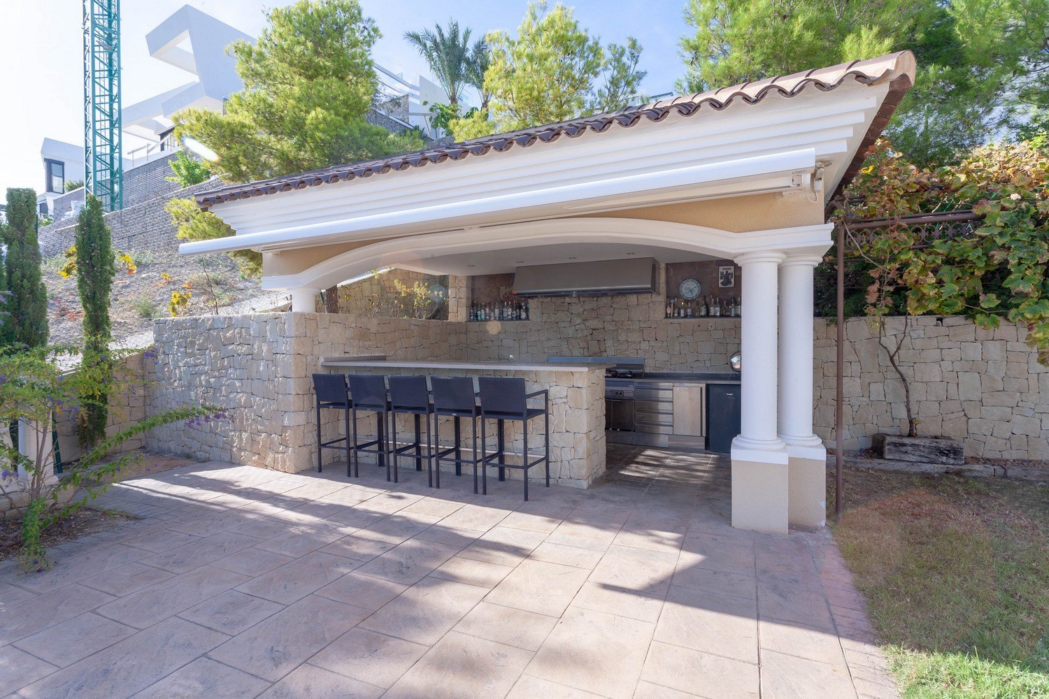Espace barbecue extérieur avec bar et tabourets dans villa à Benissa. Revêtement en pierre et comptoir en inox.