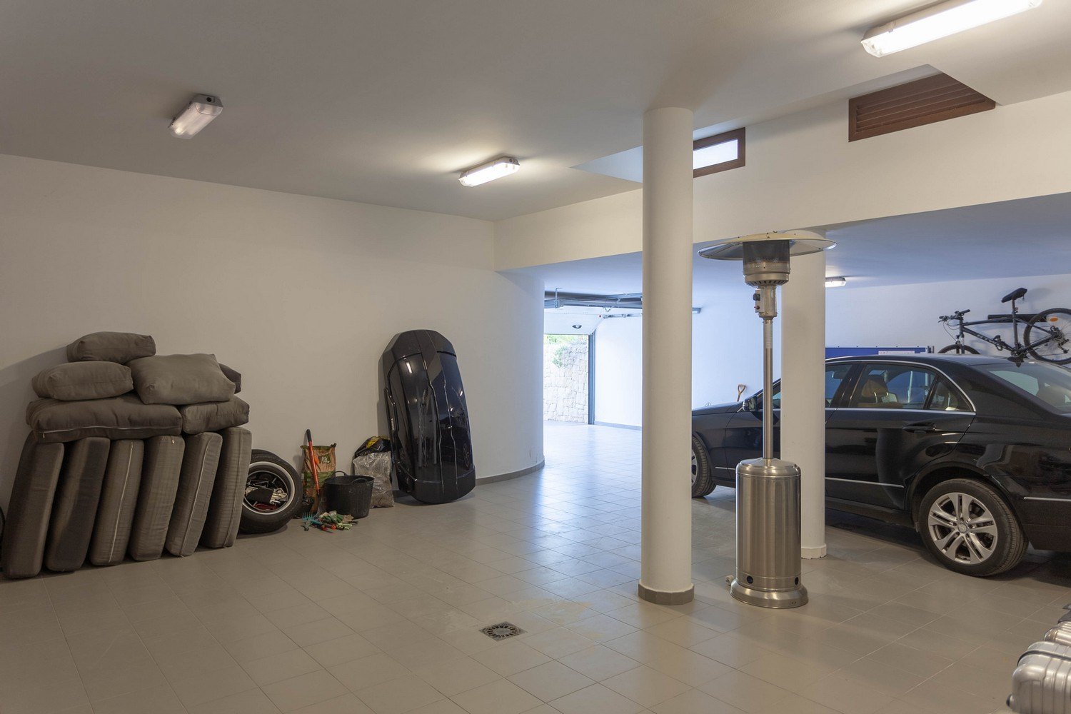 Garage spacieux avec carrelage, voiture noire et divers accessoires rangés.