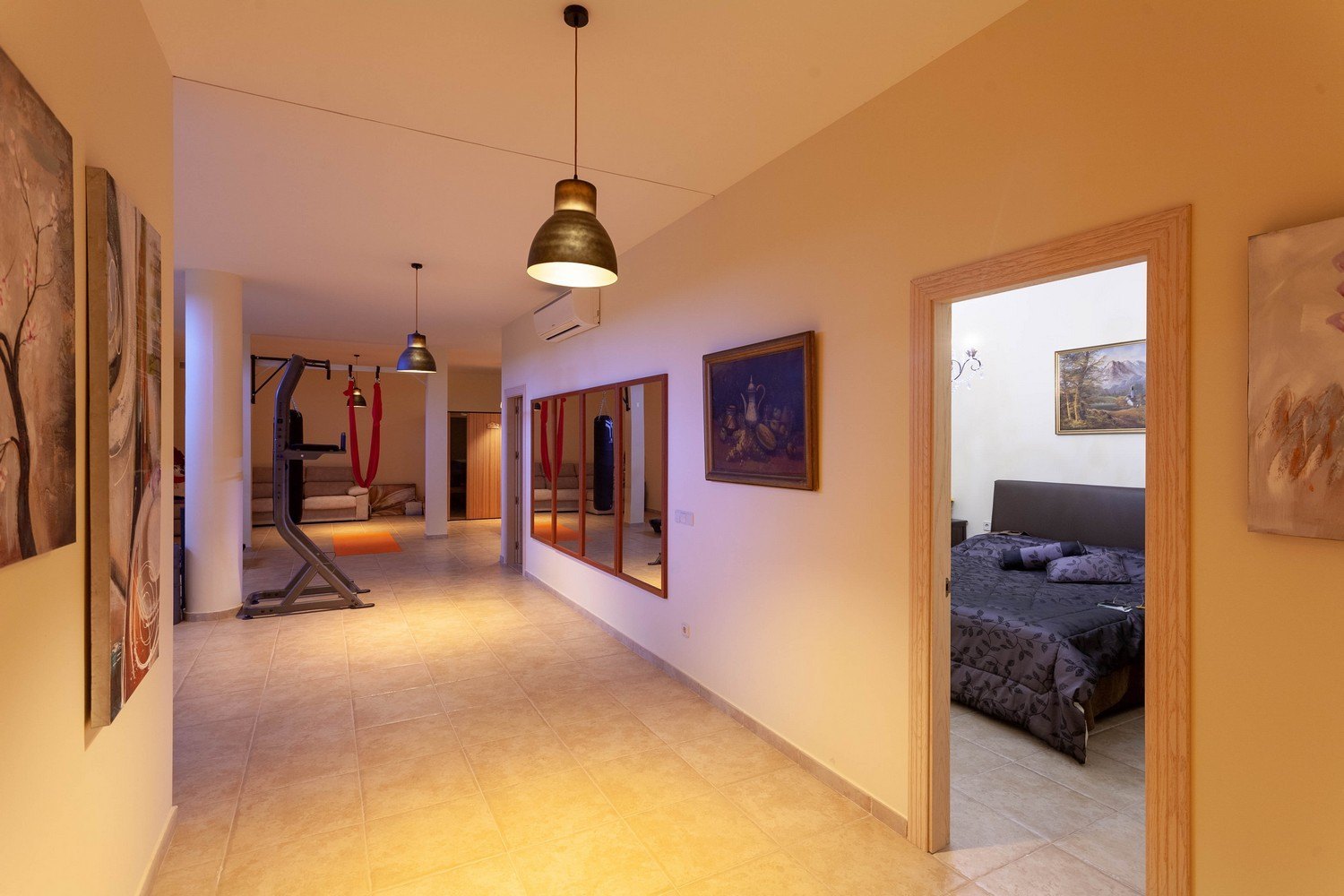 Intérieur lumineux avec salle de sport, accès sauna et entrée de chambre. Carrelage au sol et décor classique.