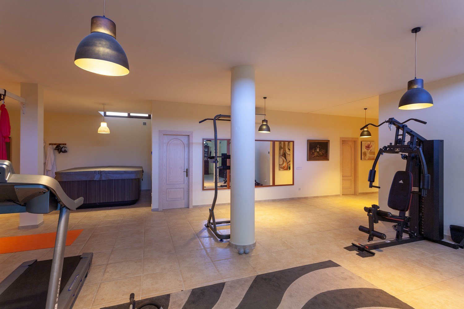 Salle de sport avec jacuzzi, carrelage crème et éclairage ambiant chaleureux.