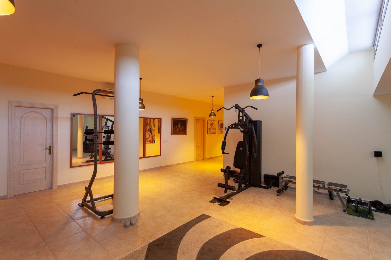 Salle de sport lumineuse avec carrelage, équipée de machines d'exercice et lumière naturelle zénithale.