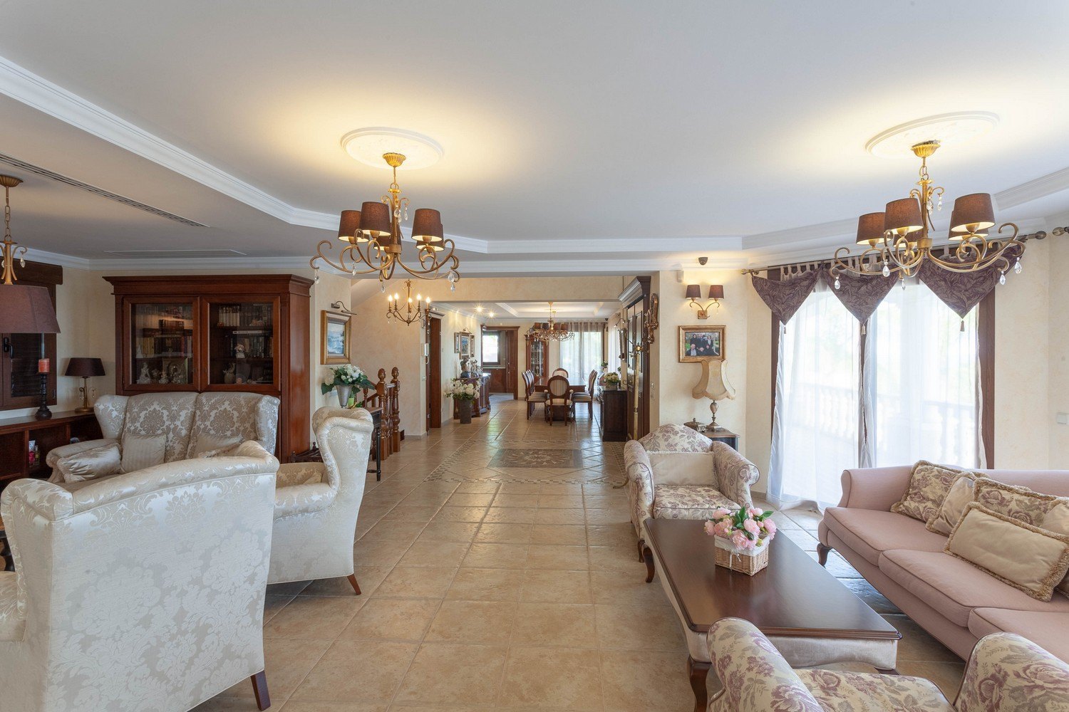 Salon à aire ouverte avec sièges rembourrés, lustres en bronze et carrelage.