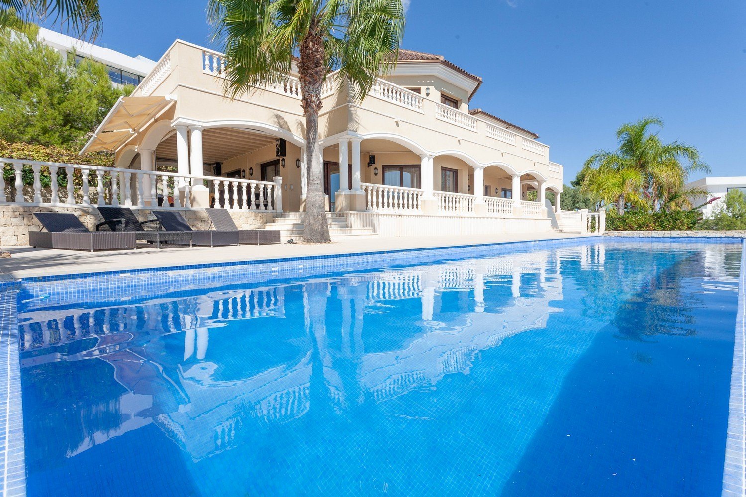 Vue sur la piscine "Infinity" carrelée de bleu et la façade de la villa méditerranéenne avec ses colonnes.
