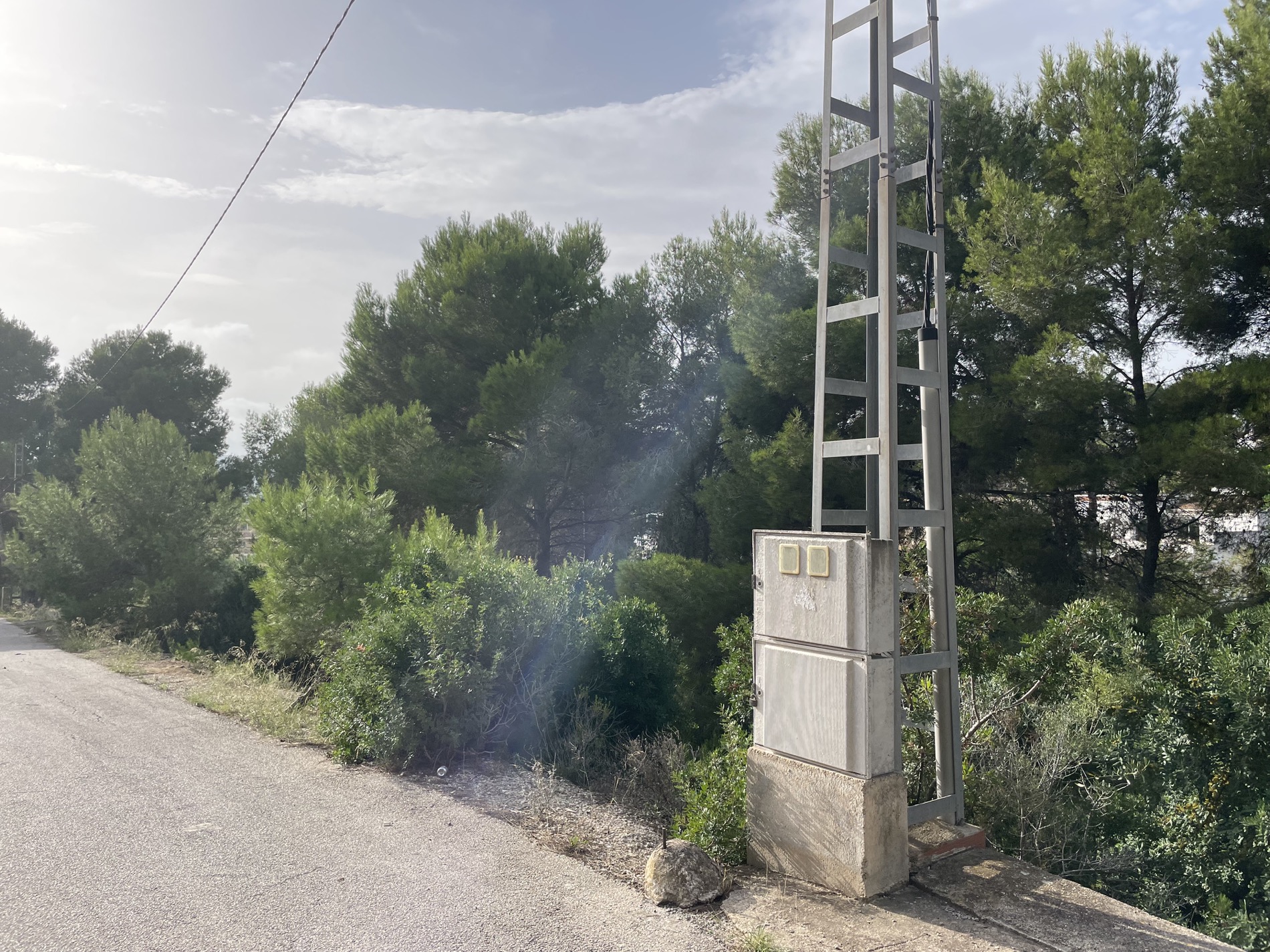 Accès routier au terrain avec infrastructure électrique installée et environnement naturel de pins méditerranéens.