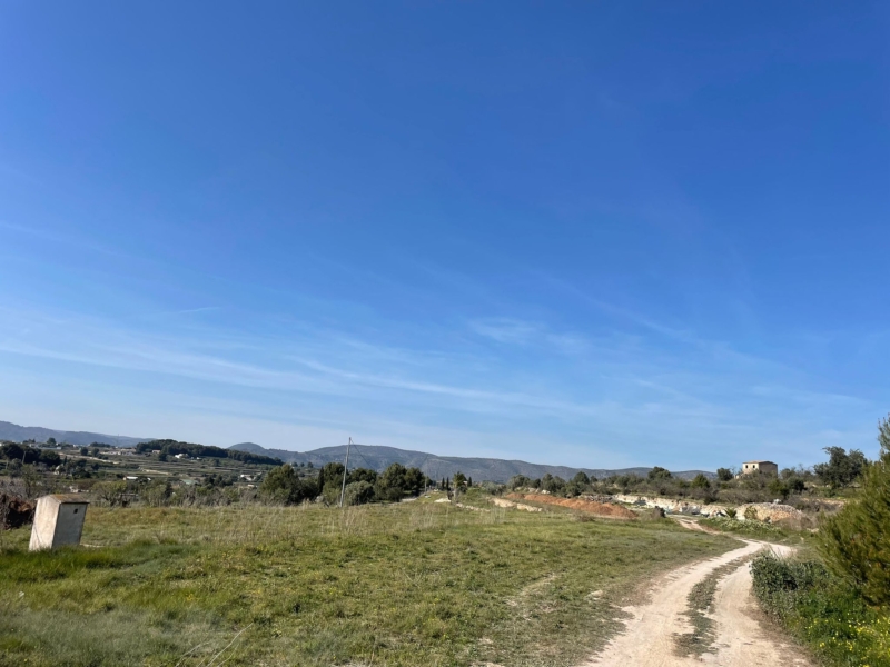 Vue du terrain avec un chemin de terre et un horizon montagneux sous un ciel bleu dégagé.