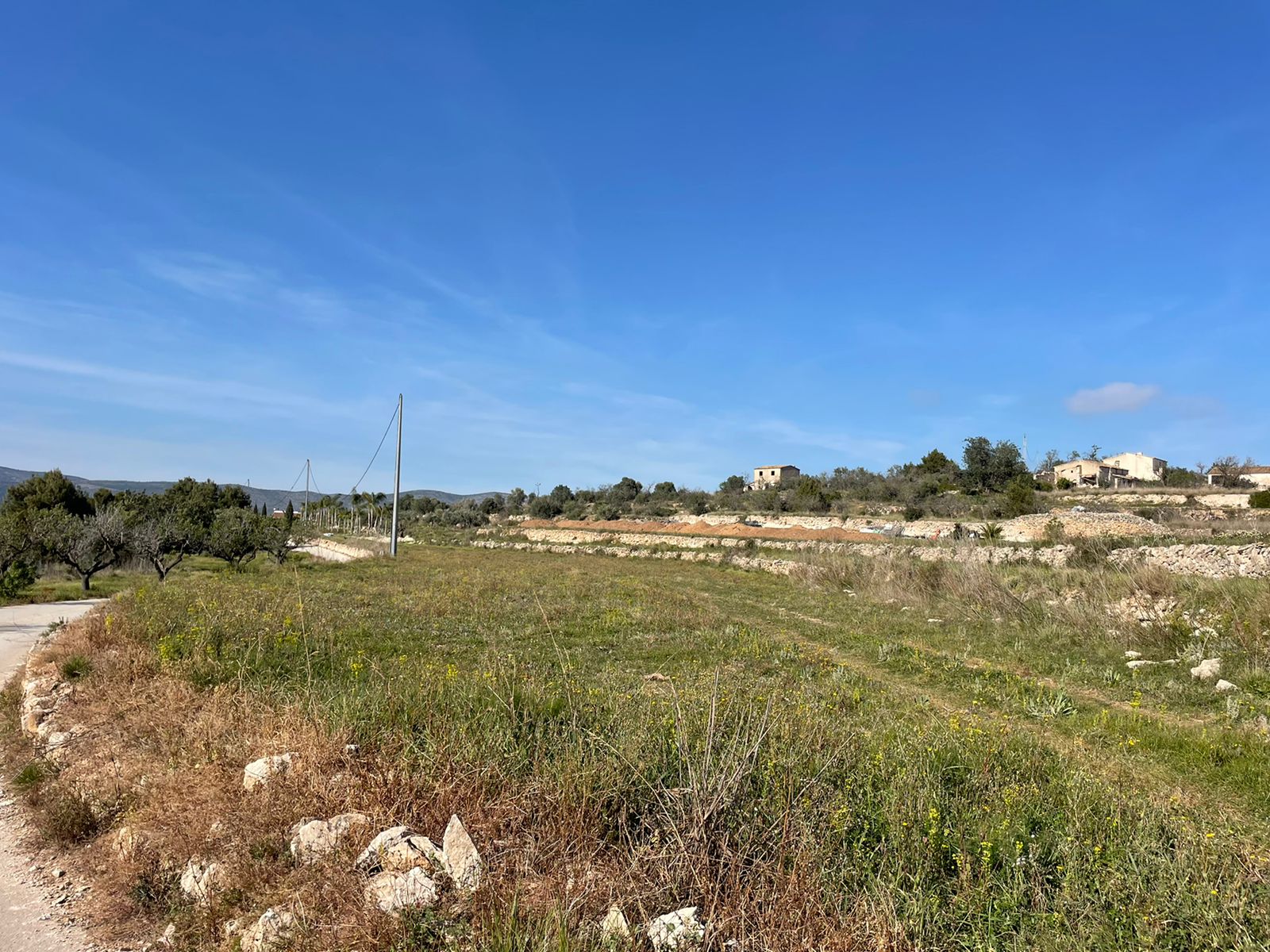 Vue d'un terrain rustique à Jávea avec des constructions surélevées et un ciel bleu dégagé.