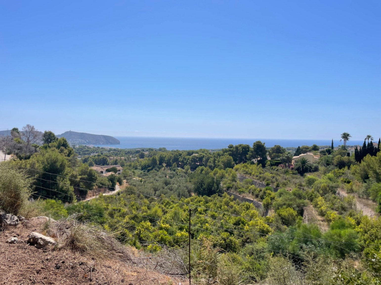 Vue panoramique depuis le terrain sur la mer Méditerranée et le Cap d'Or, surplombant une vallée verdoyante de pins et de végétation locale à Moraira.