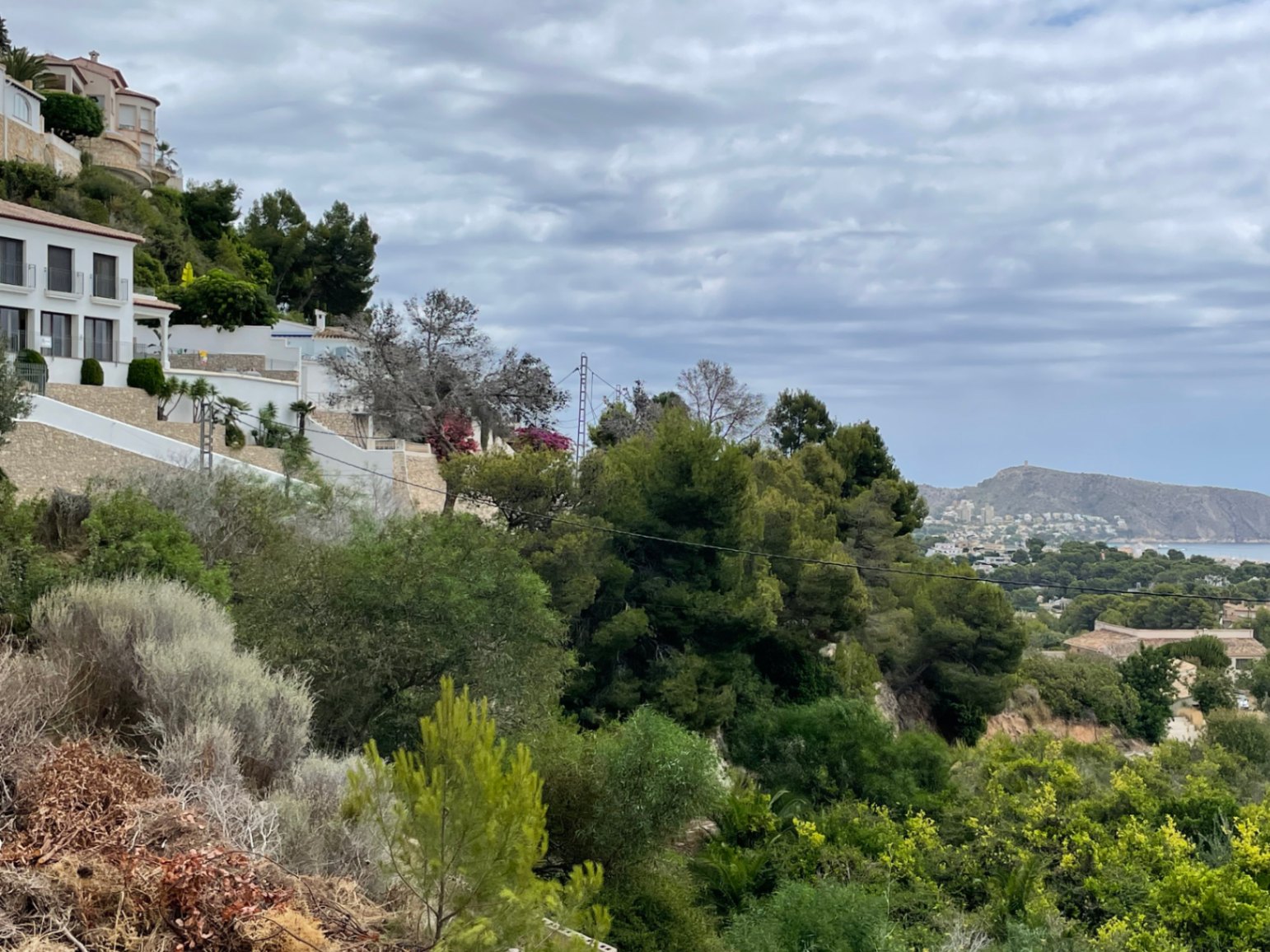 Vue surélevée depuis la colline de Benimeit, illustrant la végétation méditerranéenne, des villas aux murs en pierre et un panorama lointain sur la côte.