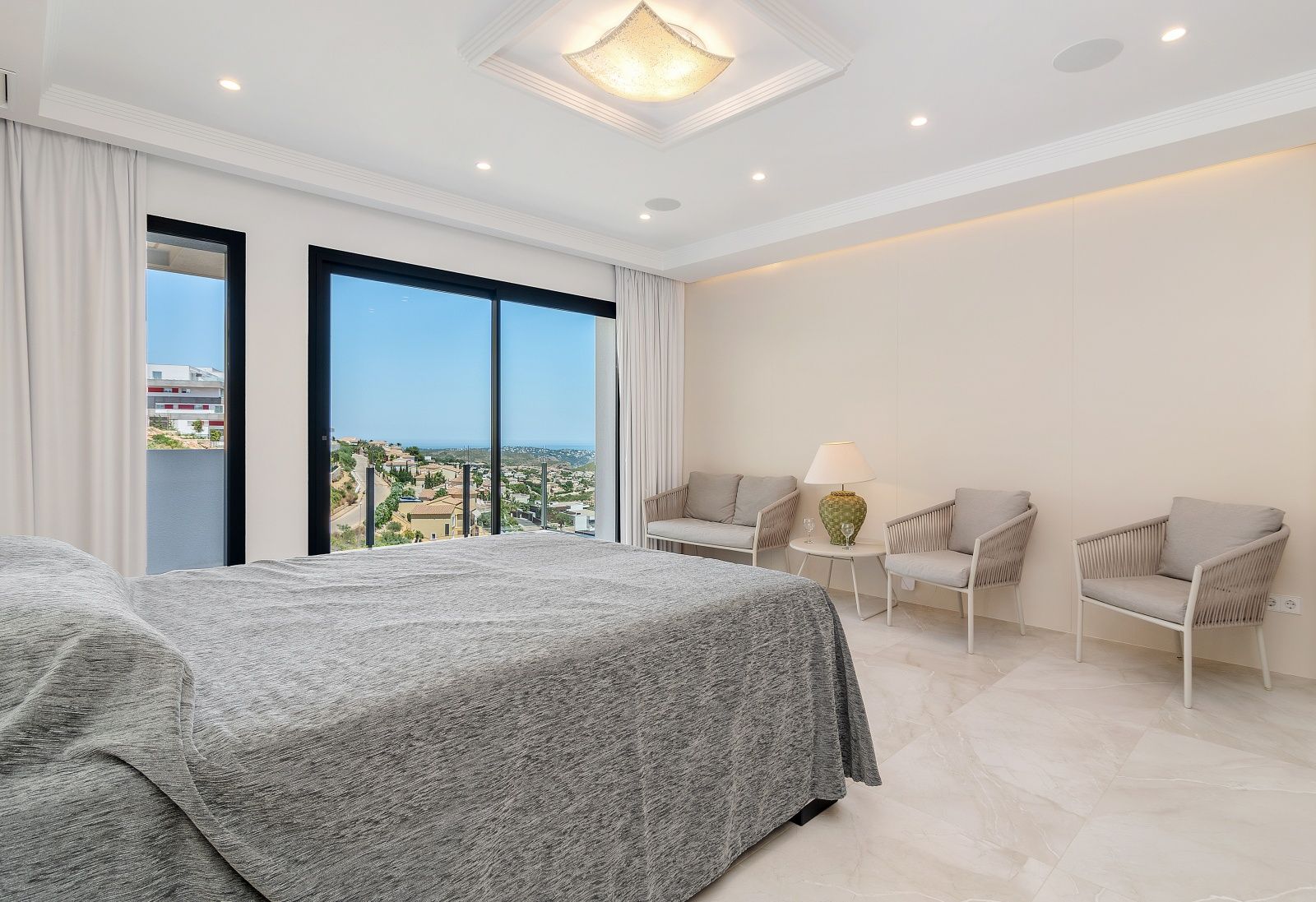 Chambre principale avec sol en marbre, coin salon intégré et grandes baies vitrées offrant une vue panoramique sur la mer et les environs.