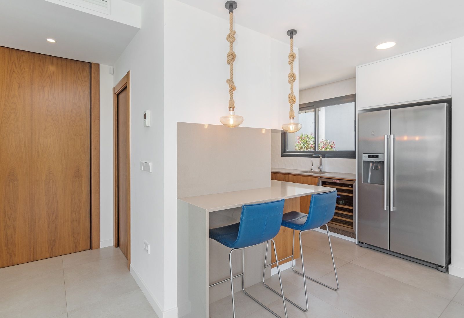 Cuisine moderne avec bar à petit-déjeuner, tabourets bleus, suspensions en corde, cave à vin intégrée et réfrigérateur américain en acier inoxydable.