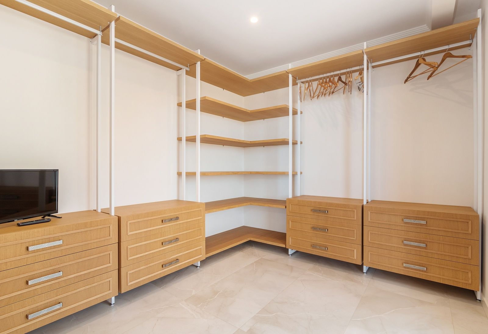 Dressing ouvert avec étagères en bois clair, blocs de tiroirs intégrés et sol en grès cérame effet marbre sous un éclairage de plafond encastré.