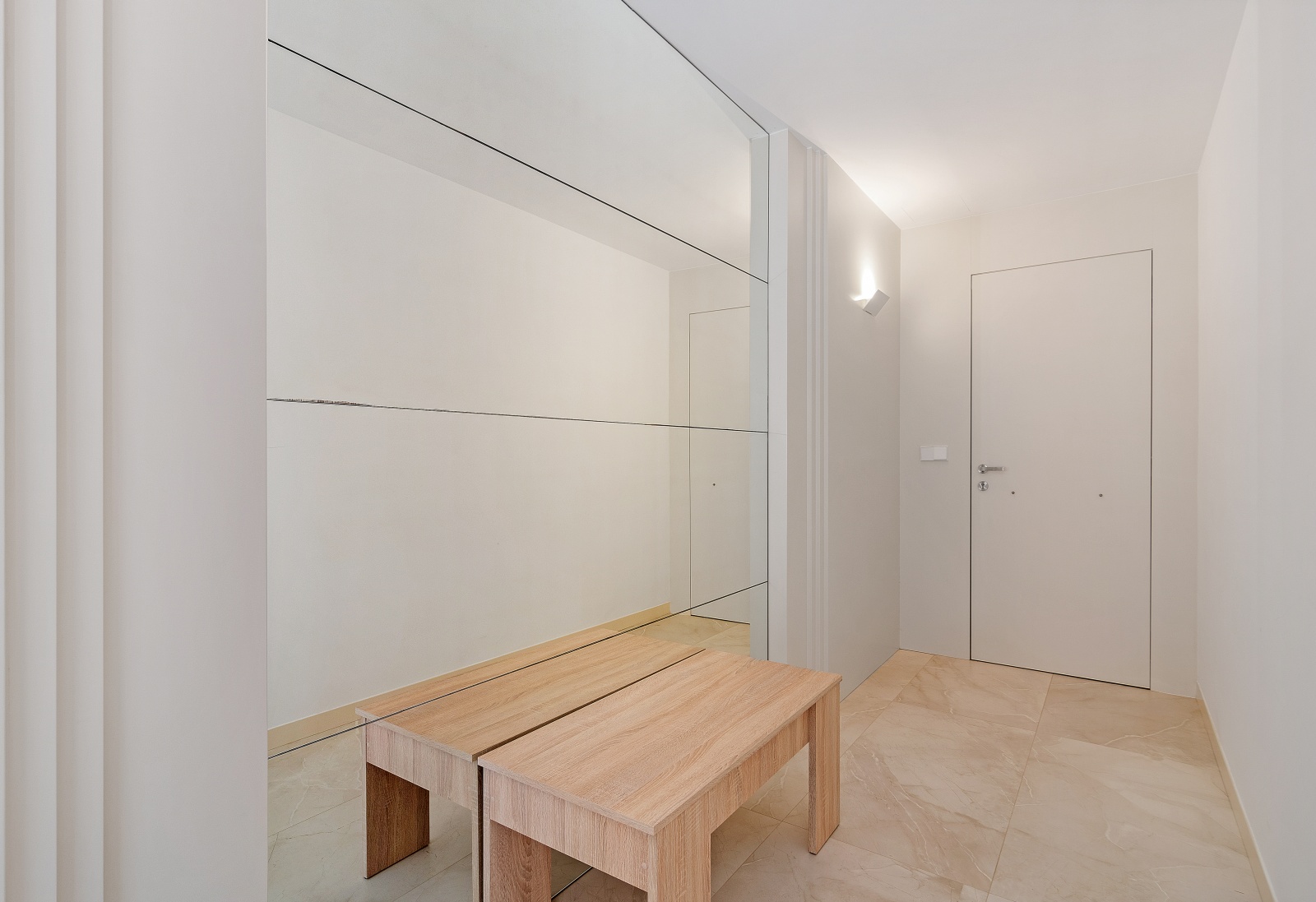 Hall d'entrée minimaliste avec un grand mur miroir, un banc en bois clair et un sol en grès cérame poli aux tons crème.
