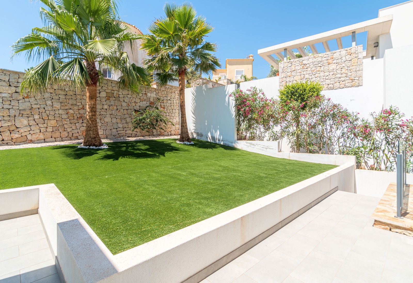 Jardin de designer à faible entretien avec gazon artificiel, palmiers et murs en pierre naturelle intégrés à l'architecture moderne de la villa.