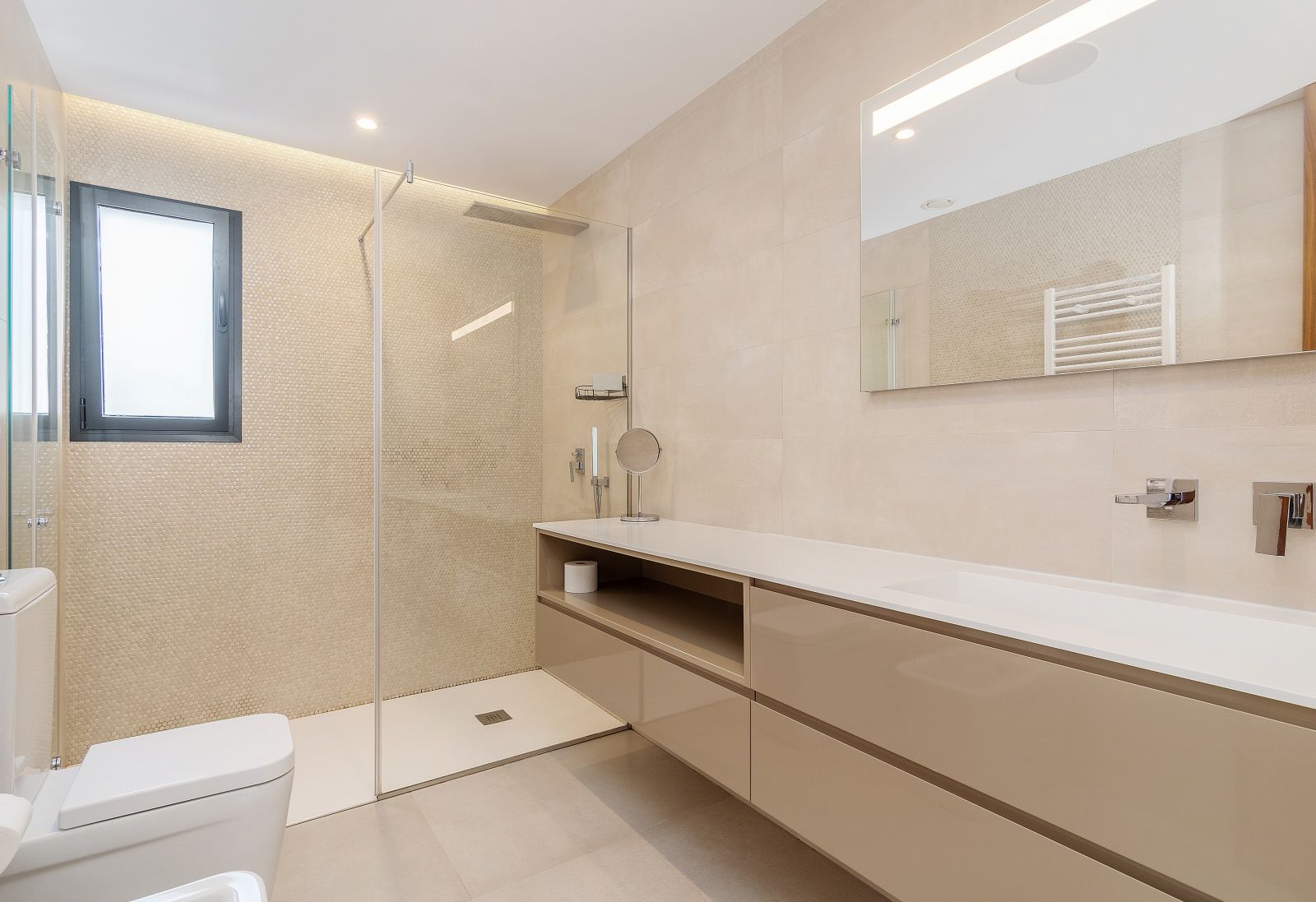Salle de bain moderne avec douche à l'italienne, paroi vitrée et mur en mosaïque. Comprend un meuble vasque suspendu beige et un miroir avec éclairage LED intégré.