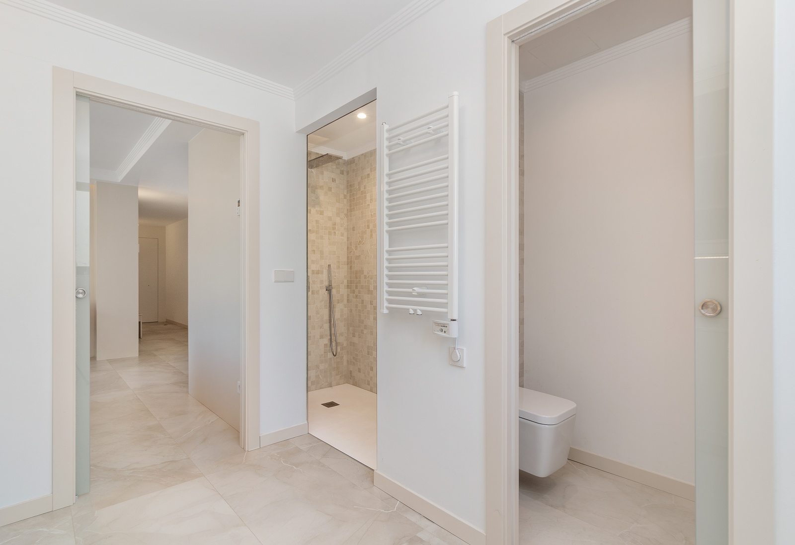 Salle de bains moderne avec douche à l'italienne en mosaïque, WC suspendu, sèche-serviettes blanc et portes coulissantes en verre sur sol en grès.