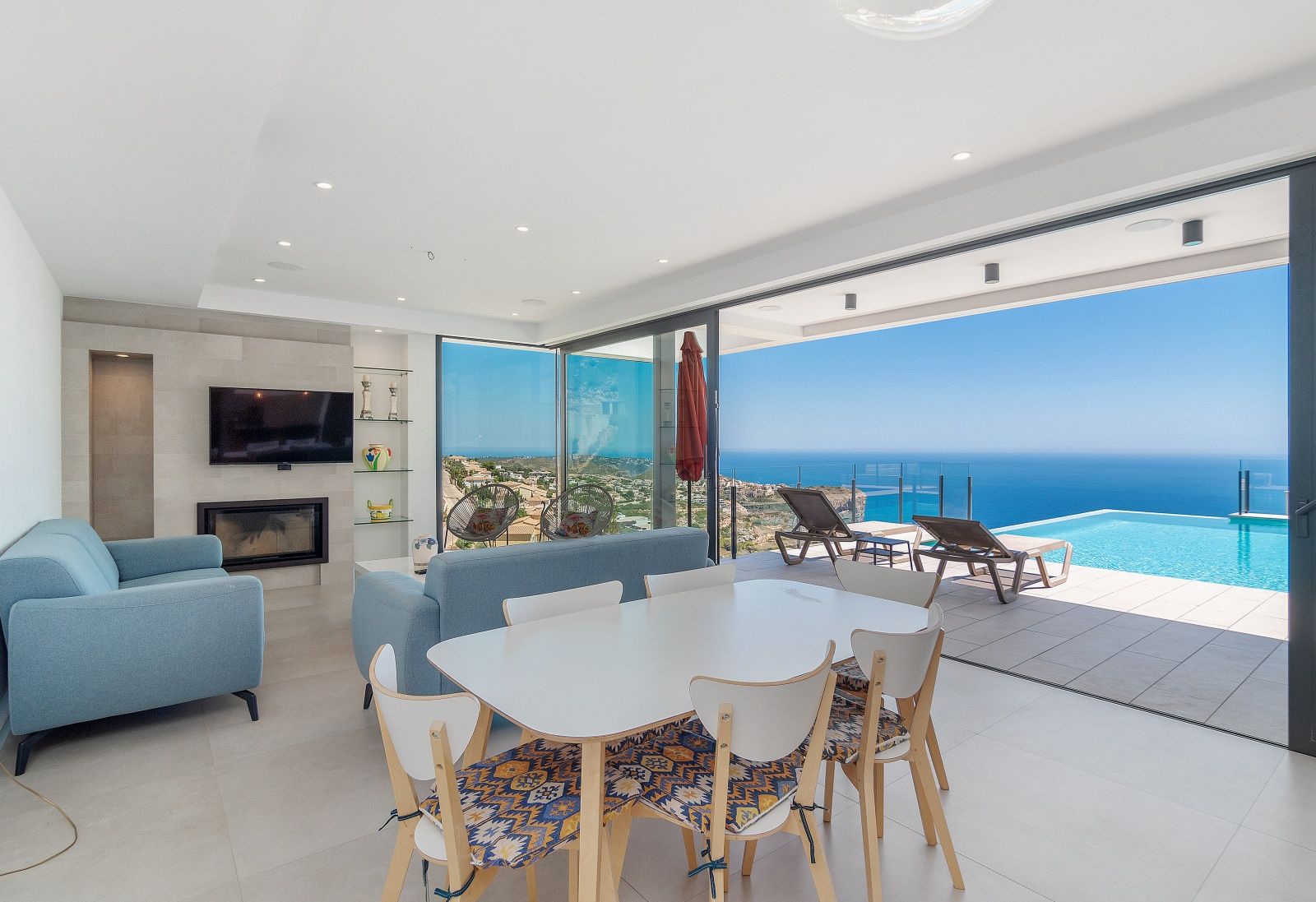 Salon-salle à manger à aire ouverte avec de grandes baies vitrées, cheminée encastrée et vue imprenable sur la piscine à débordement et la mer.