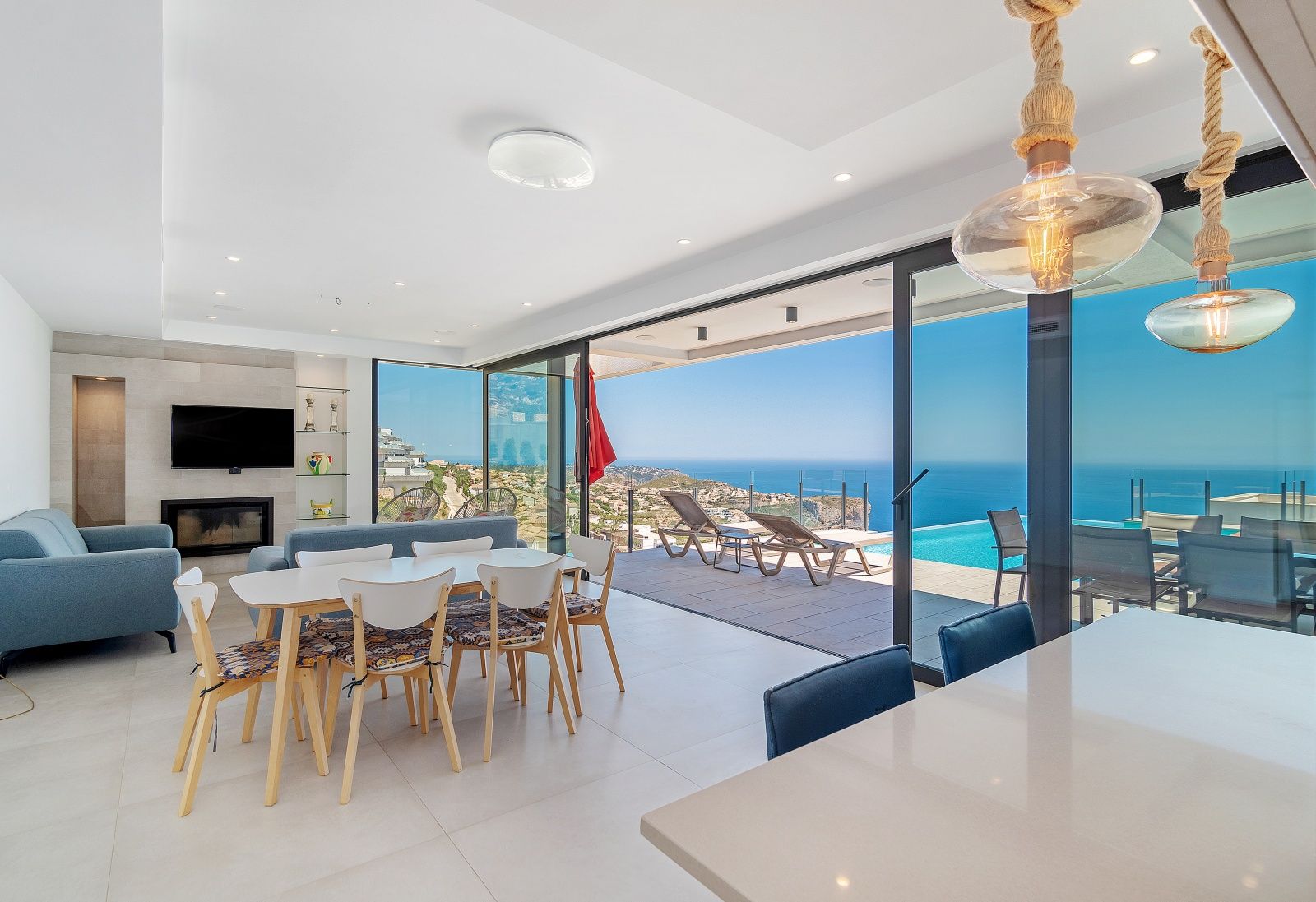 Salon-salle à manger à aire ouverte avec de grandes baies vitrées coulissantes offrant un accès direct à la piscine à débordement et une vue sur la mer.
