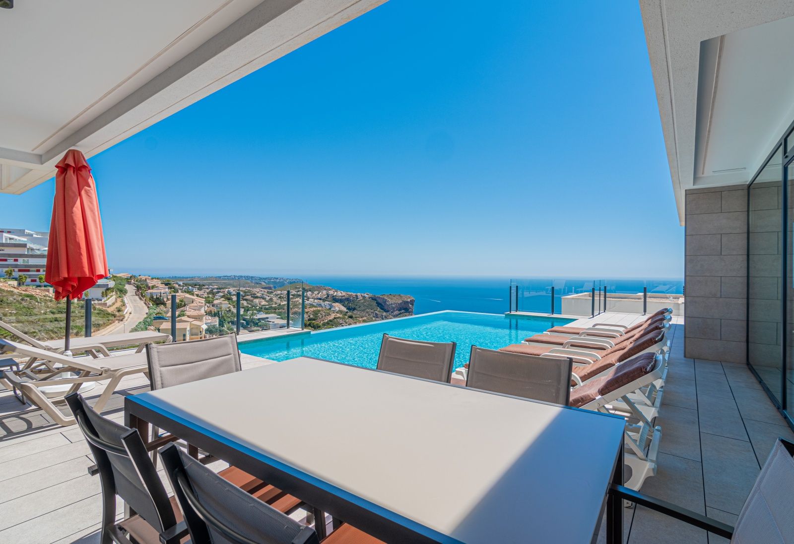 Terrasse principale avec piscine à débordement, espace repas extérieur et vue panoramique sur la mer Méditerranée et les falaises.