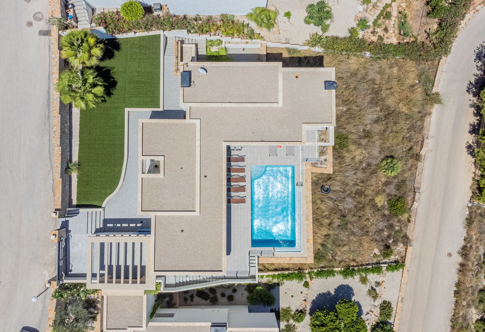 Vue aérienne zénithale de la villa moderne montrant la piscine rectangulaire, la terrasse ensoleillée et le jardin paysager avec gazon synthétique.