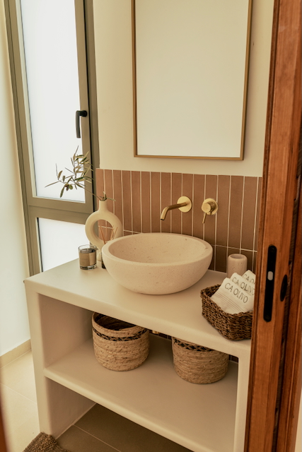 Salle de bain moderne avec vasque en pierre, robinetterie dorée encastrée et crédence en carreaux verticaux terre cuite. Meuble vasque maçonné avec paniers de rangement.