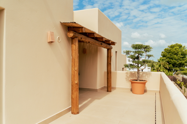 Terrasse supérieure avec pergola rustique en rondins de bois et toit en canisse, agrémentée d'un arbre d'ornement en pot de terre cuite sur un sol carrelé.