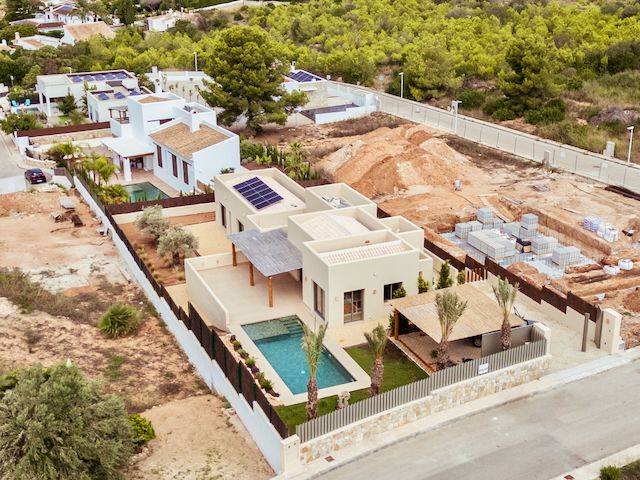 Vue aérienne de la villa moderne avec panneaux solaires, piscine privée et jardin paysager agrémenté de palmiers dans un quartier calme de Jávea.