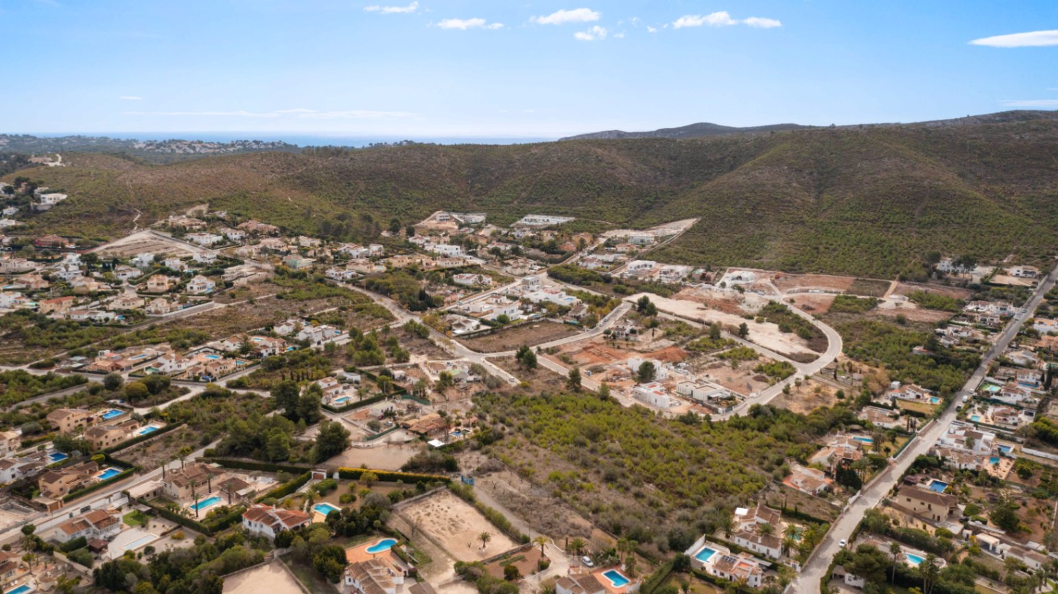 Vue aérienne du quartier résidentiel Lomas Del Rey à Jávea, illustrant l'harmonie entre les villas avec piscines et le paysage vallonné bordant la mer Méditerranée.
