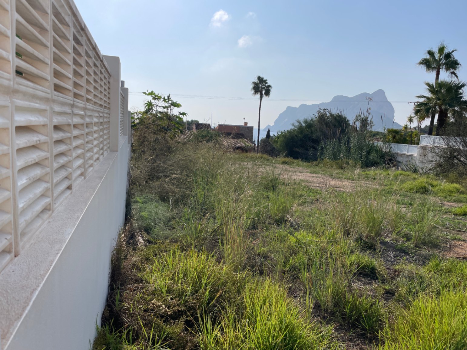 Terrain constructible de 856 m² à Bassetes, Calpe, avec mur de clôture blanc et vue dégagée sur le célèbre Peñón de Ifach à l'horizon.