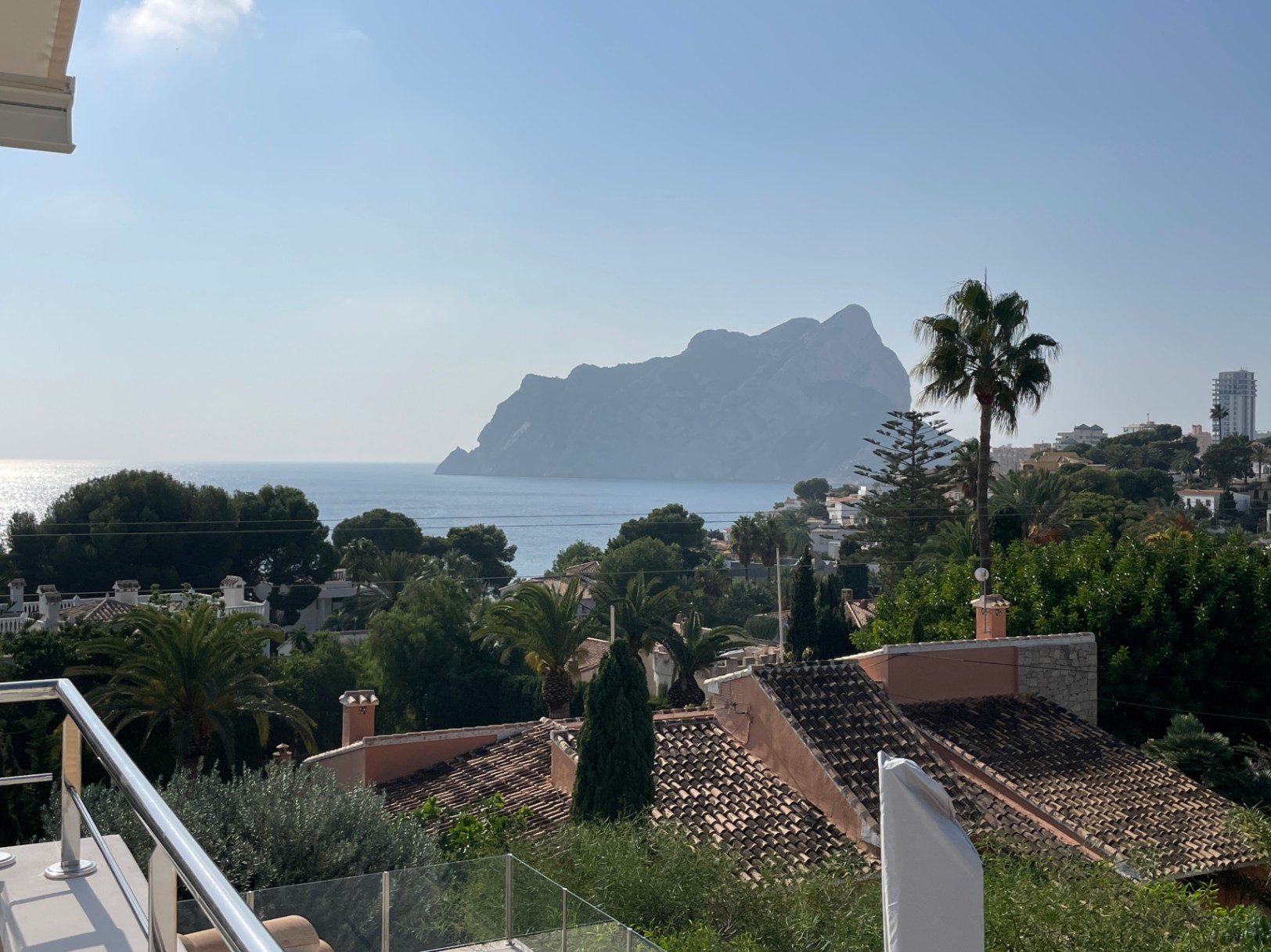 Vue panoramique depuis la terrasse sur le Peñón de Ifach et la mer Méditerranée, entourée de palmiers et de toits en tuiles traditionnels à Calpe.