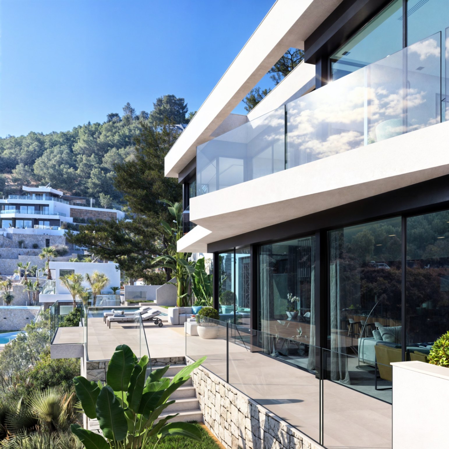 Façade contemporaine avec de larges surfaces vitrées, des garde-corps en verre et des murs en pierre naturelle sur un terrain surélevé paysager.